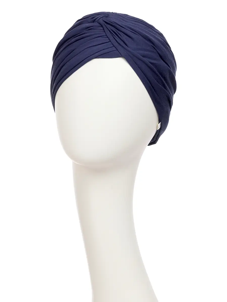 HocJoyo is a new model with a special construction that combines elegance and functionality. The model is a simple close-fitting base model with many small pleats designed to sit nicely and comfortably. A twisted, attached knot adorns the front, adding the perfect volume around the forehead and creating a subtle v-shape just above one eyebrow. This special construction ensures that volume is not only concentrated at the front but continues all the way around the back of the head. The extra fabric is easy to shape and can be moved around and placed and adjusted around as desired. Remember that you can use the HocJoyo model together with our fantastic Soft Lift Hat. It will add both extra glamor and beautiful volume around the back of your head. Here you will find the HocJoyo turban in a beautiful dark blue colour.